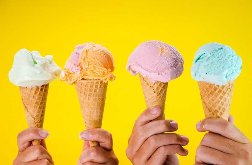 Speiseeis Hygiene für die Gastronomie: 4 Hände halten je eine Eiswaffel mit einer Kugel Eis auf gelbem Hintergrund